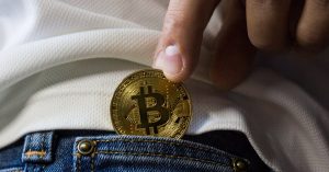 Close-up of hand putting Bitcoin in jeans pocket symbolizing cryptocurrency savings.